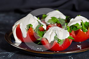 Close - up of tomato halves with finely chopped parsley in a sauce of sour cream and salt lie on a plate on a dark