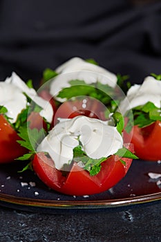 Close - up of tomato halves with finely chopped parsley in a sauce of sour cream and salt lie on a plate on a dark
