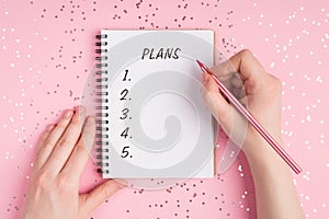 Close up top above overhead first person view photo of teen hands holding pencil and writing action plan on girly pink background