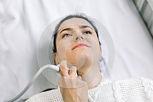 Close up top angle portrait of a young woman smiling while having her neck and thyroid examined by her doctor using