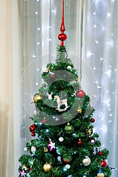 Close-up of the top of a Christmas tree decorated with toys and balls against the backdrop of a garland.