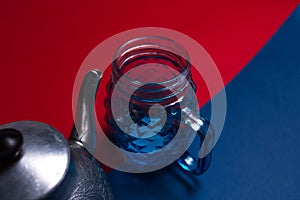 Close-up top view of aluminum teapot and glass mug on two textured backgrounds of red and blue colors