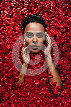 Close-up, top view, beauty portrait, face of a young woman in a bath with water and floating red rose petals and