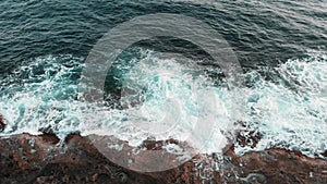 Close up top view of big white waves hitting sea rocks during storm
