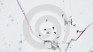 Close up top view from drone on cable way in ski resort. Ski lift elevator transporting skiers and snowboarders on snowy