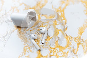 Close-up top view of earbuds charger case near wireless earphones on background of white yellow marble table.