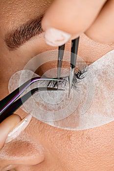 close-up top view on eyelash extension procedure. Master tweezers accurate attaches lashes