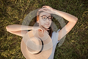 Close-up top view of a girl in the park lying on the green grass. Glasses and hat. Happy youth leisure and recreation