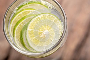 Close up top view green lime sliced in the soda water and glass place on the wooden table with blurred background