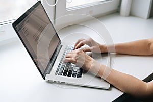 Close-up top view hands of business woman typing on laptop keyboard sitting at window sill at home, working from office.