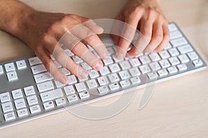 Close-up top view hands of unrecognizable business man using wireless computer keyboard sitting at light working desk in