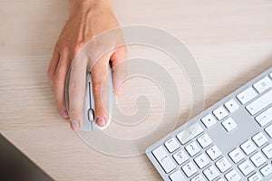 Close-up top view hands of unrecognizable business man using wireless computer mouse sitting at desk with white modern