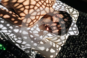 Close-up top view of handsome young man relaxing lying down with closed eyes on massage table in sunlight and beautiful