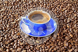 Close-up and top view of hot black coffee in blue coffee cup and roasted Thai coffee beans on wooden background.