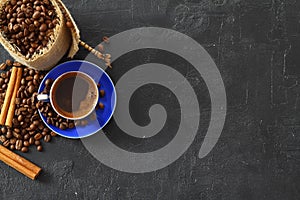 Close-up and top view of hot black coffee in blue coffee cup and roasted Thai coffee beans on wooden background.