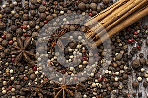 Close-up top view image with multi-colored pepper seeds, cinnamon sticks