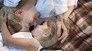 Close-up top view loving mother and daughter rubbing noses lying on blanket in summer spring park. Happy Caucasian woman