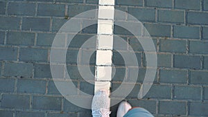 Close-up, top view. male legs in white sneakers go along the white line of road markings.