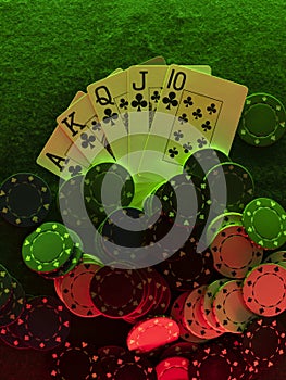 Close-up top view photo of royal flush and chips laying on green cover of playing table, against black background, under