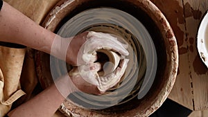 Close-up top view of potter`s hands with working with wet clay on a pottery wheel making a clay product in a workshop