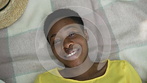 Close-up top view relaxed African American woman laughing looking at camera lying on blanket outdoors. Portrait of happy