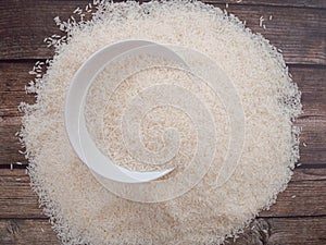 Close up top view rice in a white bowl and scattered near on wooden table with copy space for text and design