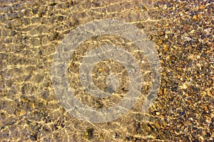 Close-up and top view of shiny transparent yellow sand and stones on the beach with clear water. clear sea, the river