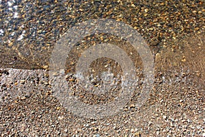 Close-up and top view of shiny transparent yellow sand and stones on the beach with clear water. clear sea, the river