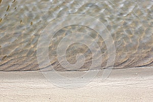 Close-up and top view of shiny transparent yellow sand and stones on the beach with clear water. clear sea, the river