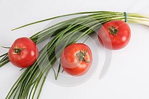 Close up top view shot of a bunch of green onions and three ripe red tomato on a white background