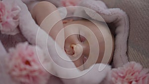 Close-up top view sleeping infant girl lying in cozy bed with pink flowers. Cute Caucasian baby with closed eyes