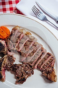 Close up top view of sliced charcoal grilled wagyu T-Bone steak served with BBQ sauce in white plate.