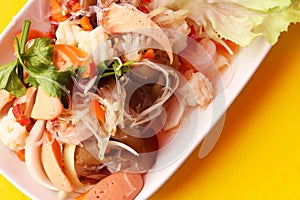 Close up top view spicy salad of vermicelli and seafood in white plate on yellow background, Thai food Yum Woon Sen