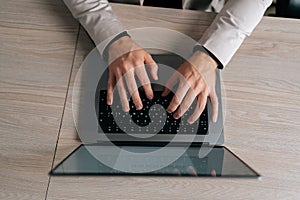 Close-up top view of unrecognizable businessman in suit working on laptop computer by window. Closeup male fingers