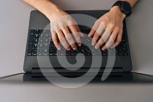 Close-up top view of unrecognizable businessman wearing smartwatch typing on laptop computer sitting at desk in office.