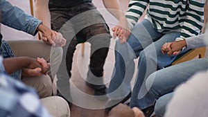 Close-up top view of unrecognizable multi-ethnic and different ages people sitting in circle and holding hands