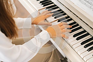 Close-up top view of unrecognizable musician female pianist playing gentle music on white classical piano in light