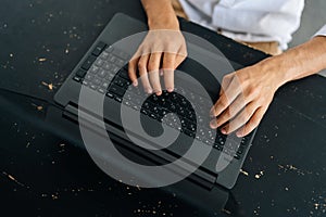 Close-up top view of unrecognizable young man typing texting on modern laptop keyboard, male employee sitting at black