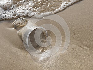 Close up top view of a Waste transparent plastic cup on the sand beach, a moment before rushed by sea wave, with copy space