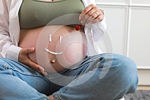 Close-up of torso of young pregnant model applying moisturizer on her belly to avoid stretch marks. Future mom with