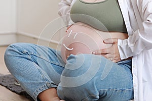 Close-up of torso of young pregnant model applying moisturizer on her belly to avoid stretch marks. Future mom with