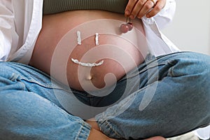 Close-up of torso of young pregnant model applying moisturizer on her belly to avoid stretch marks. Future mom with