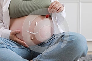 Close-up of torso of young pregnant model applying moisturizer on her belly to avoid stretch marks. Future mom with