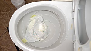 Close-up tossing a dirty baby diaper into the toilet. It clogs the toilet flush