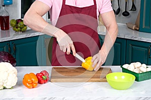 Close up of tough guy cutting paprika at kitchen. Chef`s hands with knife