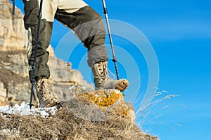 Close-up of a tourist`s foot in trekking boots with sticks for Nordic walking standing on a rock stone in the mountains