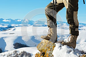 Close-up of a tourist`s foot in trekking boots with sticks for Nordic walking standing on a rock stone in the mountains