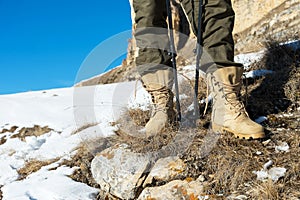 Close-up of a tourist`s foot in trekking boots with sticks for Nordic walking standing on a rock stone in the mountains
