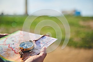 Close-up tourist& x27;s hand holds compass with magnetic arrow showing north direction, over map against lighthouse