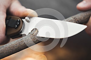 Close-up of the tourist`s hands, sharpening a stick with a knife. The concept of travel, extreme and survival